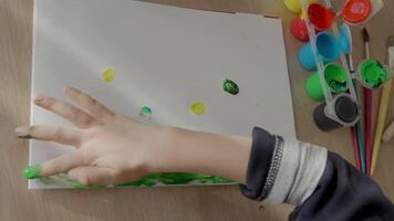The boy paints with his fingers on a sheet of paper, creating colorful patterns. A 4-5-year-old European boy enjoys finger painting at home, exploring creativity and textures video