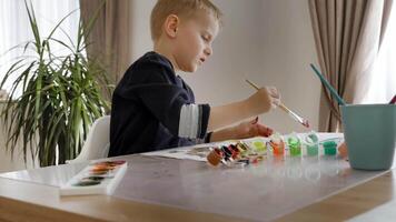 A young European boy, around 4-5 years old, is creating artwork with acrylic paints on paper. He sits at home, enthusiastically exploring colors and shapes video