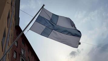 Finnish national flag waving in the wind against a soft evening sky, mounted on a building in an urban setting video