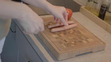 Hands cutting sausage on wooden cutting board. Concept of cooking process and meal preparation video