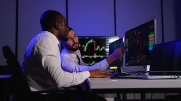 Two investment fund analysts analyze stock market charts on multiple monitors in office video