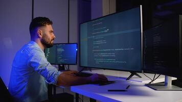 Programmer writing code on multiple screens in a dark office video