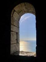Sea view through the oval window of the stone tower. Sea surface illuminated by the evening sun. photo