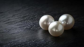 Elegant arrangement of three shimmering pearls on black stone surface photo