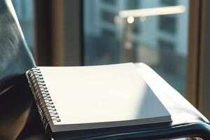 Spiral-bound blank notebook placed on a chair by the window with sunlight illuminating the pages photo