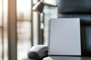 Blank spiral notebook on leather chair in bright office environment photo