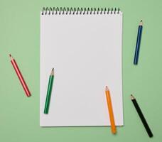 Open notebook with white blank sheets and wooden pencils on green background, top view photo