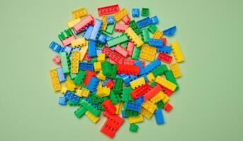 Scattered plastic multi-colored parts of children's construction set on green background, top view photo