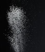 Close-up of white granular particles sugar, falling against a black background. High contrast and detailed texture of the grains photo