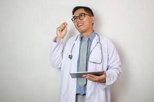 waist up asian physician looking up information on the tablet computer is touching his face while thinking with a serious expression in the office. photo