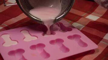 Liquid pink wax is poured into a mold to shape the penis, which has been prepared with a wick inside. making wax candles at home. Close up video