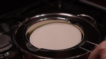 A large piece of butter or white chocolate is placed in a saucepan and placed in a water bath to begin the melting process. Close up. video