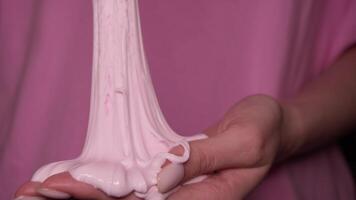 The jelly - like pinkish substance shimmers and stretches in the teenager 's hands . A toy made of slime. In slow motion. video