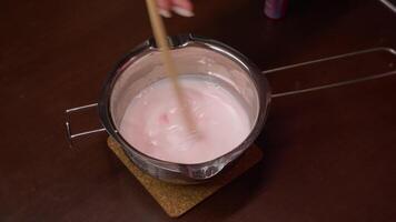 Artisan mixes the melted wax with red dye in a pan, using active movements of a stick. As a result, the mixture gradually turns pink. video