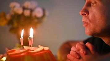 Close up of man making a wish with clasped hands before blowing out candles on a birthday cake Anniversary Valentine Day decorated with orange slices video