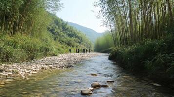 A serene river scene surrounded by lush bamboo and mountains, with people walking along the bank. photo