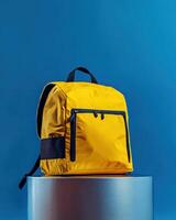 A bright yellow backpack on a pedestal against a blue background, showcasing modern design photo