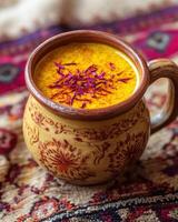 A decorative mug filled with golden beverage topped with saffron, set on a patterned fabric. photo