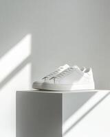 A pair of stylish white sneakers displayed on a pedestal with soft lighting. photo