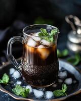 A glass pitcher filled with iced coffee, garnished with mint leaves on a dark background. photo