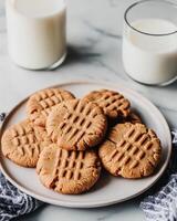 A plate of peanut butter cookies with glasses of milk, inviting a cozy snack moment. photo