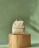 A minimalist beige backpack on a wooden pedestal against a green background photo