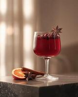 A glass of red beverage garnished with spices and orange on a table. photo