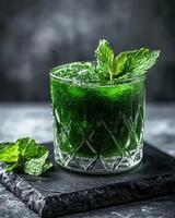 A refreshing green drink garnished with mint leaves, served in a crystal glass photo
