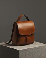 A sleek brown leather backpack displayed on a stone pedestal against a dark background. photo