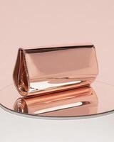 A sleek, rose gold clutch bag displayed on a reflective surface, ideal for evening events photo