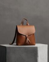 A stylish brown leather backpack displayed on a concrete pedestal against a neutral backdrop. photo