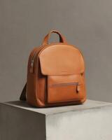 A stylish tan leather backpack displayed on a pedestal against a neutral background. photo