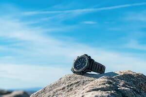 A black watch rests on a rocky surface under a clear blue sky. photo