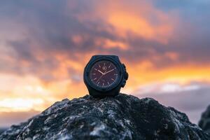 A black watch resting on a rock against a vibrant sunset sky. photo