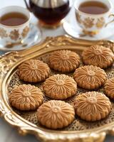 A beautifully arranged tray of floral-patterned cookies with cups of tea in the background. photo