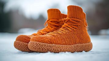 An orange knit shoe is sitting on top of snow photo