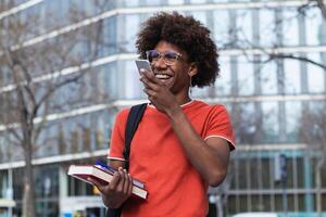 Joyful young black guy sending voice message via smartphone while standing on street after studies photo