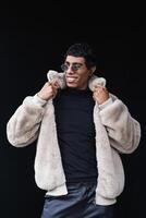 Smiling trendy ethnic man in sunglasses on black background photo
