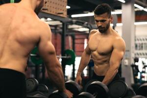 strong man standing in front of the mirror taking dumbbells in a gym photo