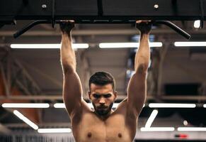 front view of a strong man doing pull ups in a gym photo