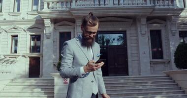 A Stylish Man is Engaged in Using a Smartphone While Standing in Front of an Elegant Building video