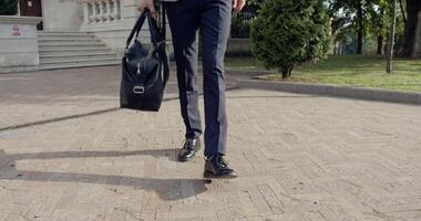 A focused businessman is confidently walking while holding a briefcase on a modern paved path video