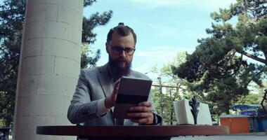 A businessman is using a tablet while enjoying his time in an outdoor cafe setting video
