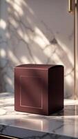 Elegant plum box with gold detail, set against marble and gentle sunlight. Perfect for luxury packaging, presentation, or high-end product. photo