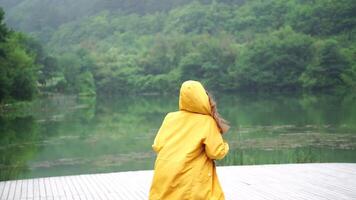 A woman in a yellow jacket stands on a lake, looking out at the water. The scene is peaceful and serene, with the woman's reflection in the water adding to the sense of calm. video