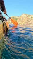 Kayaking sea adventure. Person paddles yellow kayak in daytime at ocean, near mountain, for recreation. video