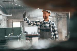 Showing thumb, up. Factory male worker in uniform is indoors photo