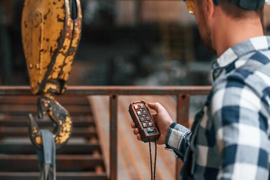 Using the controller with buttons to operate the little crane machine. Factory male worker in uniform is indoors photo