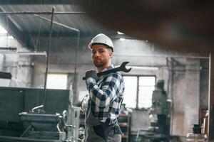 Standing and holding ,wrench. Factory male worker in uniform is indoors photo