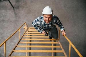 Top view. Going up on the ladder. Factory male worker i,n uniform is indoors photo